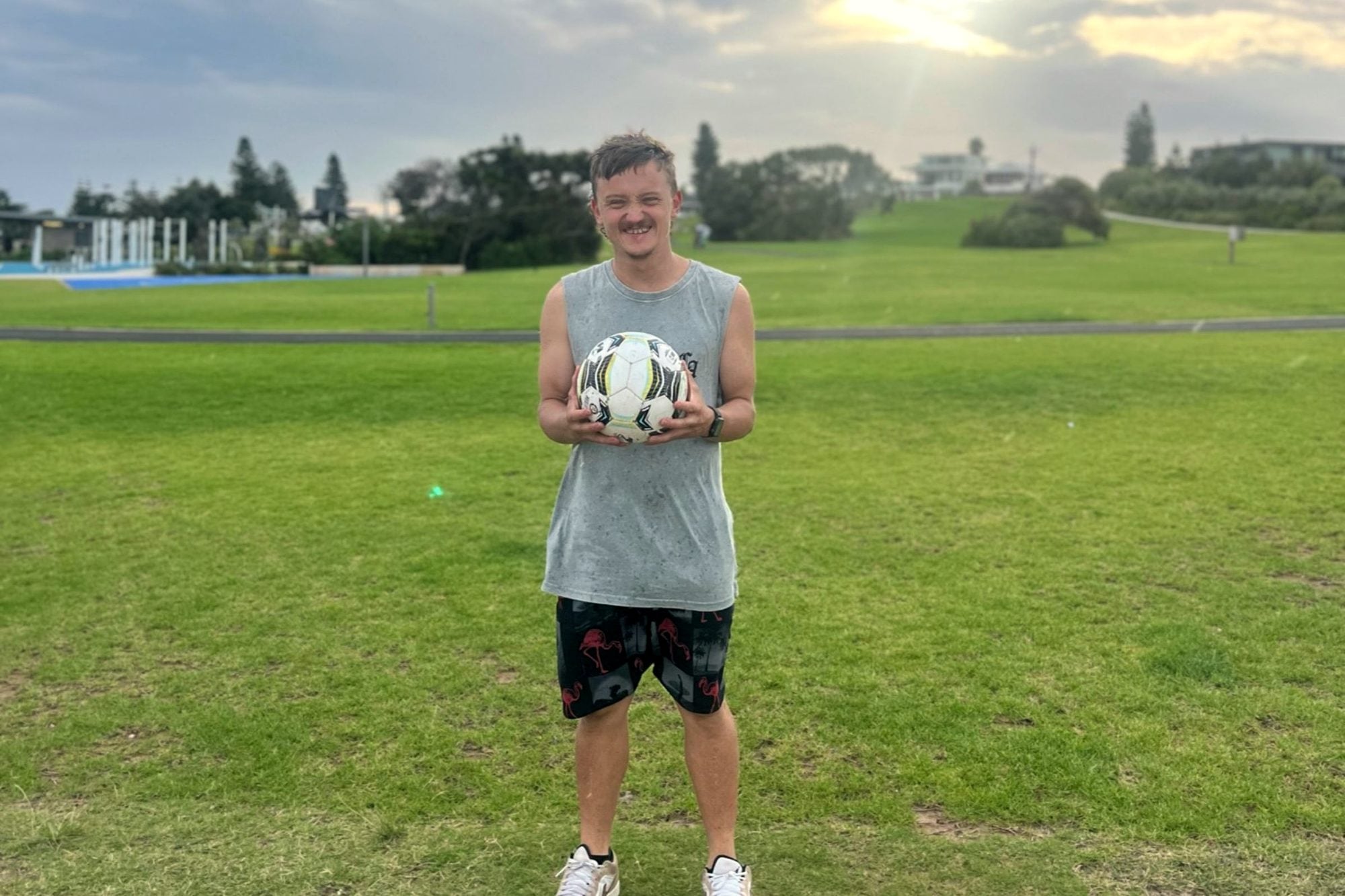 A smiling person holding a football in a park