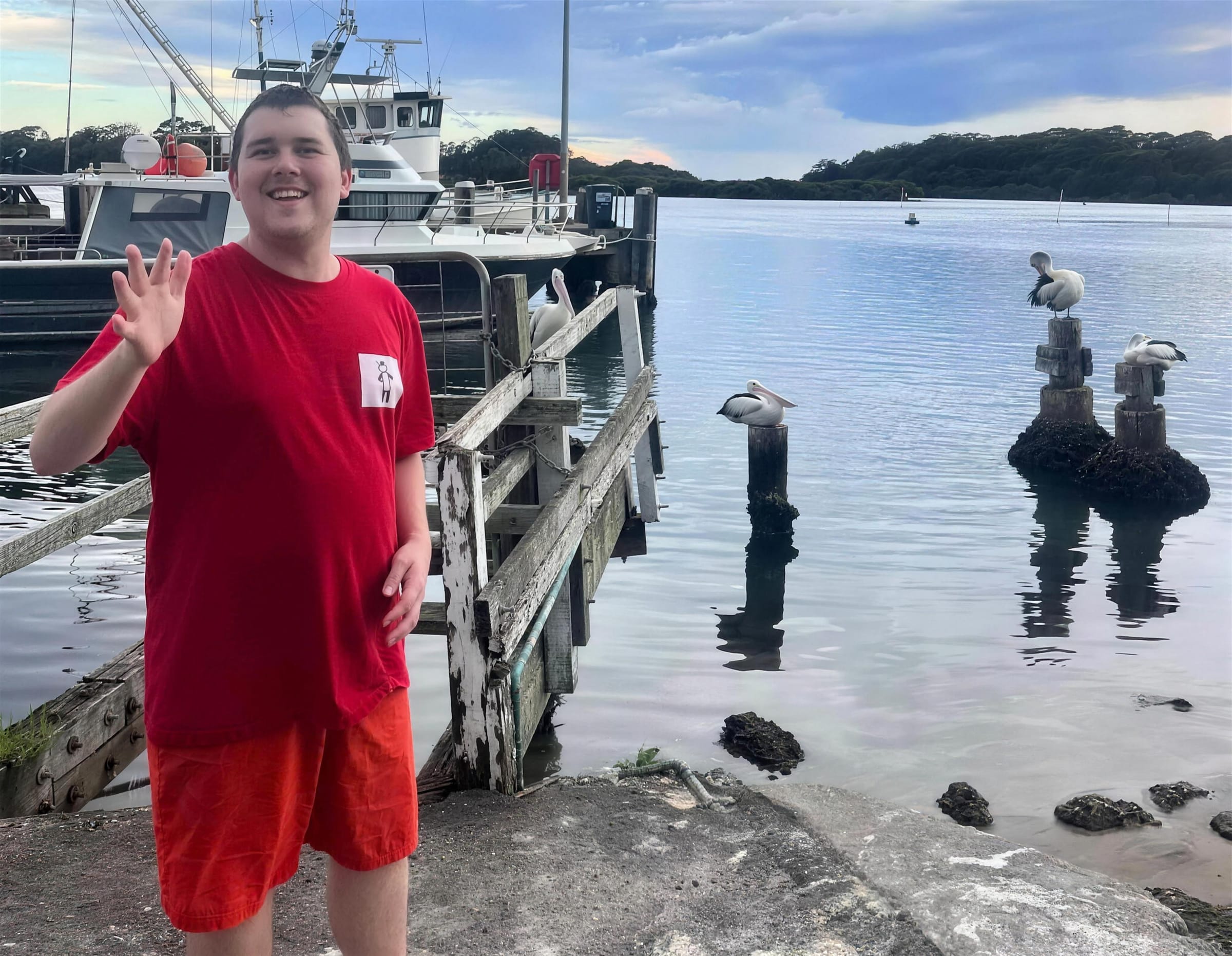 A smiling person waving beside the water